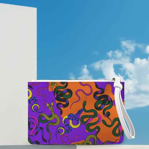 Rectangular wristlet clutch featuring vibrant purple and orange background with colorful snake prints. White strap and gold zipper visible.